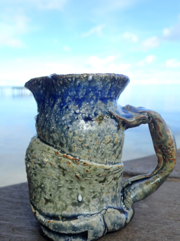 This medium small pitcher is hand thrown on the potter's wheel and slighty altered with a sculpted Japanese style handle. It is made with stoneware or Japanese style clay and glazed in blue and yellow Huahine lagoon glaze. Each picture is unique